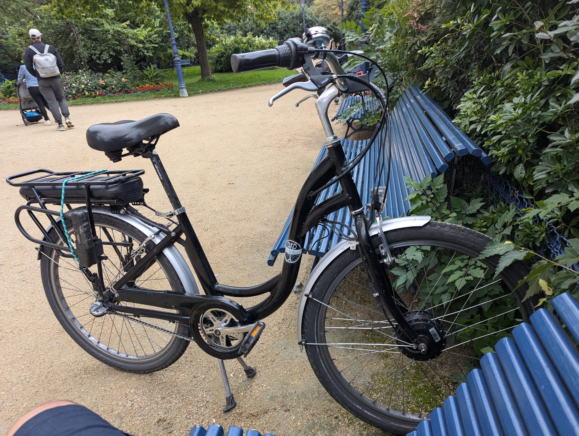 Electric bicycle parked between two benches at a park up against a bush